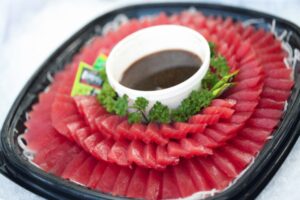 A black tray full of sliced Fresh Ahi Tuna with a bowl of soy sauce in the middle