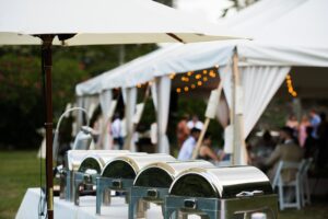 Wedding reception Setup with Silver Food warmers placed on top of a catering table and under an umbrella