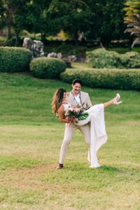 A groom holding his bride up for a photoshoot on a lush green lawn