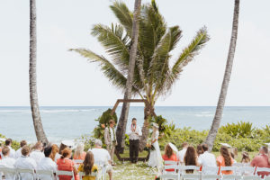 A couple getting married in a scenic waterfront ceremony, exchanging vows with a breathtaking view of the water as their backdrop surrounded by lovedones captured by Rachel Kathryn