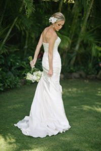 Bride with flowers in her hair, holding her Dress while walking in a tropical garden