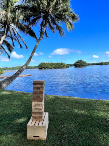 Aloha Taps' Big Jenga placed next to a coconut tree on a lawn by the water