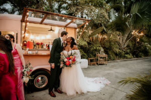 A bride and groom at a tropical garden wedding, kissing in front of Gazoz mobile bar