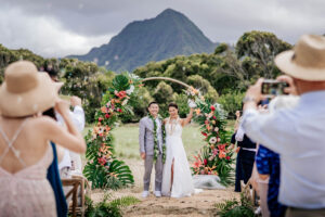 A Wedding Couple Smiling during their Wedding Ceremony against beautiful mountains at Kualoa Ranch, captured by HNL Studios