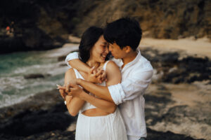 A couple with their faces close together as they share an intimate moment against a beach in Hawaii captured by Seeking Films