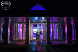 A romantic moment captured by Shannon Sasaki Photography as a couple kisses in front of a building illuminated by blue and purple lights