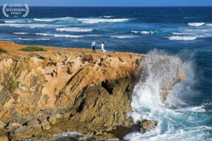 A couple walking on top of a cliff surrounded by crashing waves and the ocean